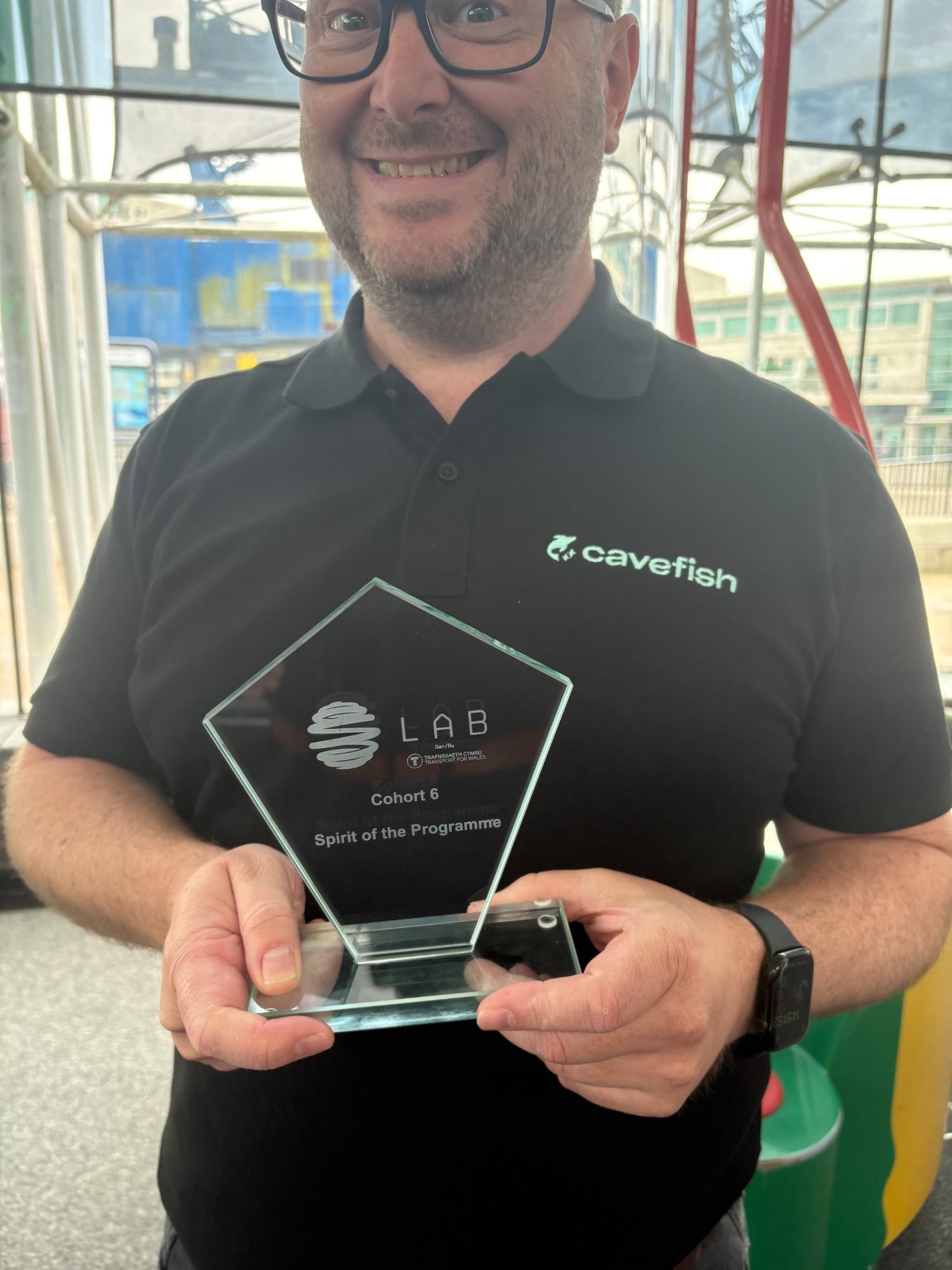 Cavefish Cohort 6 Spirit of the Programme award from the TfW LAB accelerator by Transport for Wales — a glass pentagon trophy held by a Cavefish team member wearing the Cavefish logo polo shirt.